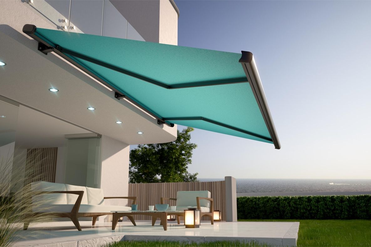 Türkise Markise an moderner Hausfassade über Terrasse mit Sitzmöbeln und Blick aufs Meer