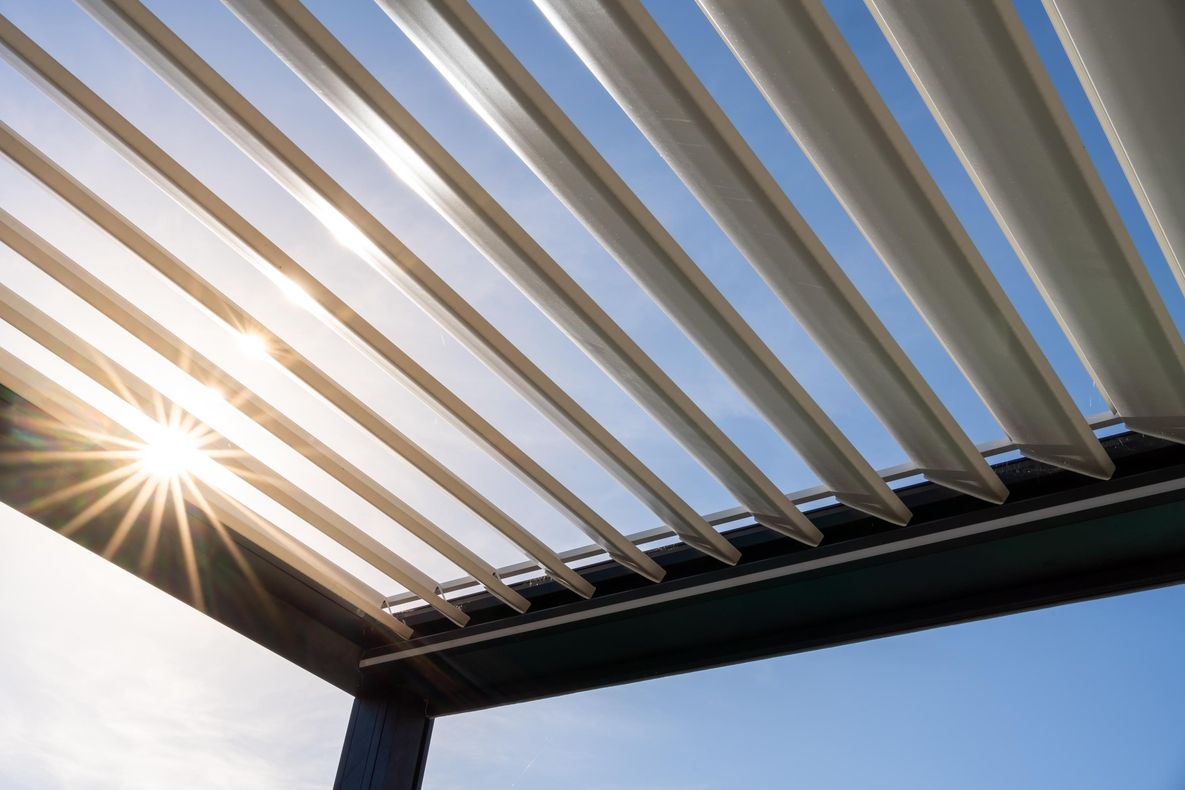 Sonnendurchlässige Lamellen einer Terrassenüberdachung mit Sonnenstrahlen im Hintergrund